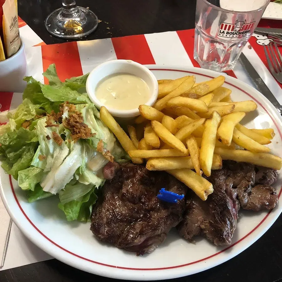 Entrecôte frites salade photographiée au téléphone en salle, couverts et verre dans le cadre